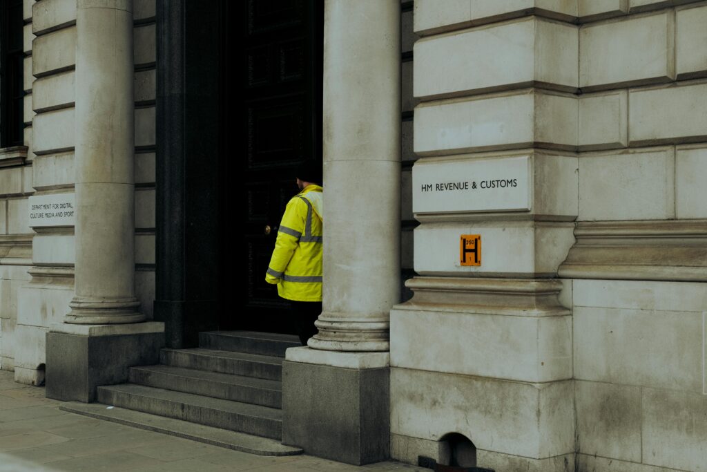 A guard in yellow jacket at the entrance of HM Revenue & Customs building in the UK.